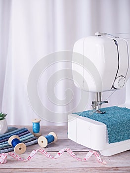 Sewing machine working with blue fabric, sewing accessories on the table, stitch new clothing