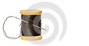 Sewing needle with black thread stuck in wooden spool with black threads close up isolated on white