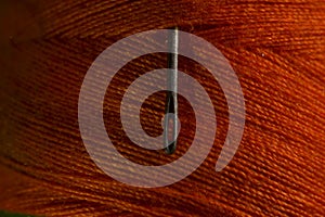 sewing needle on orange bobbin thread