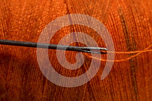 sewing needle on orange bobbin thread