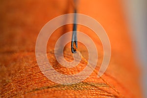 sewing needle on orange bobbin thread
