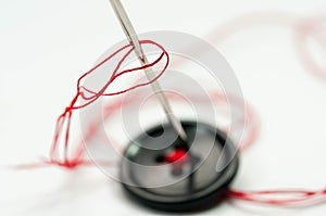 Sewing needle with red thread, black button close up macro shot