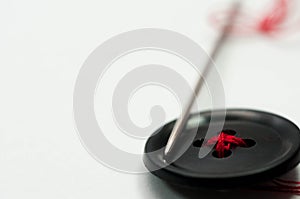 Sewing needle with red thread, black button close up macro shot