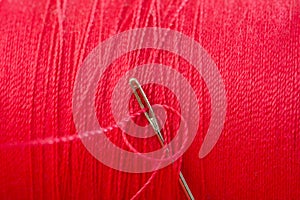 Sewing needle on red thread spool background