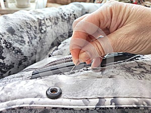 Sewing with a needle and thread on a mottled spotted fabric by hand. A middle-aged or mature hand with a sewing needle