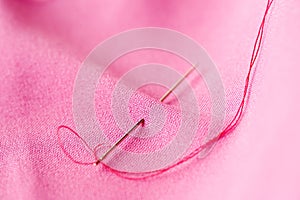 Sewing needle with thread stuck into pink fabric