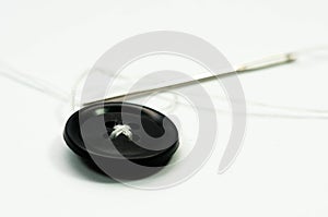 Sewing needle with white thread, black button close up macro shot