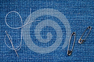 Sewing needle with a white thread and two pins on a denim fabric
