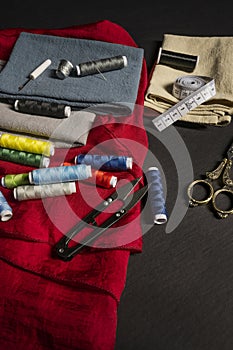 Sewing objects with vintage golden metal scissors, various needles, thimbles, red cloth, spools of colored threads, cloth,
