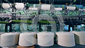 Sewing spools are mechanically unwinding at a textile factory.