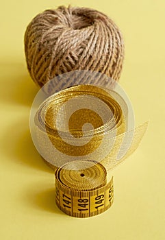 Sewing supplies. Twine, gold ribbon and tailor`s meter on yellow background. Vertical format