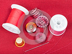 Sewing thread, buttons, thimble on red tissue
