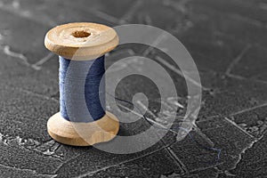 Sewing thread on an old wooden spool with dark concrete background