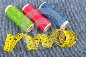 Sewing threads in green  red and blue colors and a yellow measuring tape on blue denim in blur.Soft focus.Ð¡oncept of sewing