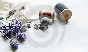 Sewing tools with fresh lavander flowers on linen background. Vintage wooden spool, braid, thimble, buttons.