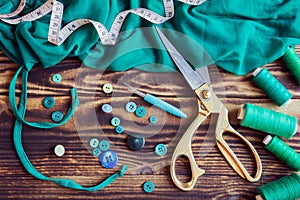 Sewing tools, green fabric, threads and buttons on a wooden background