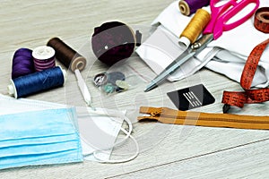 Sewing tools : scissors, colorful bobbins with thread and gel, medical mask on wooden table.