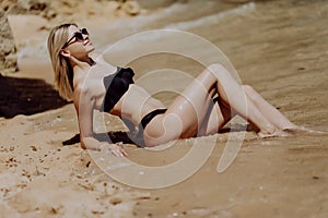 Sexual blonde girl take sunbath on the beach. happy female with black swimwear, enjoying summer holidays