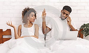 African workaholic husband ingnoring his iiritated wife in bed photo