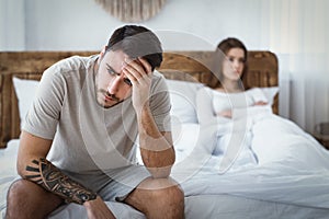 Sexual dysfunction. Husband holds his head, upset wife on bed photo