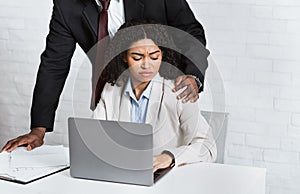 Sexual harassment in office. African American boss molesting his female employee at workplace