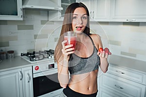 Sexual sports girl holding a bowl of strawberries and a glass of smoothie in the kitchen.