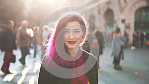 Sexy Asian hipster looks at the camera and smiling in the middle of a crowded street. Cute girl with pink colored hair