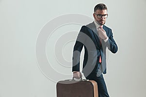 Sexy bearded man in his forties holding luggage and fixing tie