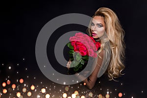 beautiful blond model in elegant dress holding a bouquet of red roses. Valentines`s gift on a black background