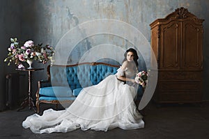 and beautiful brunette model girl in stylish and fashionable lace wedding dress with naked shoulders sits on the antique sofa