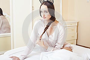 Sexy beautiful brunette woman lying in bed sensual, looking at camera. Seduction concept in luxury room interior