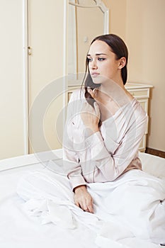 Sexy beautiful brunette woman lying in bed sensual, looking at camera. Seduction concept in luxury room interior