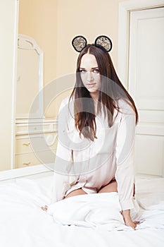 Sexy beautiful brunette woman lying in bed sensual, looking at camera. Seduction concept in luxury room interior