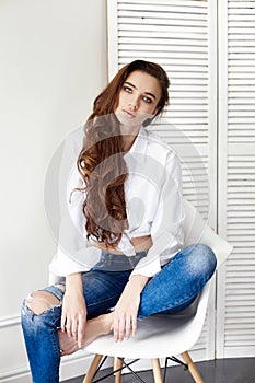 beautiful girl in jeans white shirt sitting on a chair. Gorgeous long hair and charming eyes young woman. Business lady