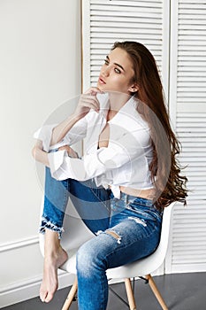 beautiful girl in jeans white shirt sitting on a chair. Gorgeous long hair and charming eyes young woman. Business lady