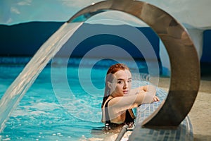 sexy beautiful reddish woman in black bath costume relaxing in the swimming pool of a spa centre