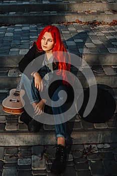 Sexy beautiful redhead girl with magnificent long hair. Ukulele playing, sitting on the steps in the park. Perfect woman portrait