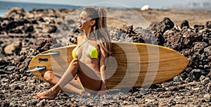 Sexy beautiful surfer girl on the beach relaxing after surfing. Tanned woman with fit body. Rocky coast. Hobby. Sport