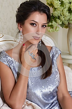 beautiful young brunette woman with evening make-up chic groomed wearing a short evening dress embroidered with silver