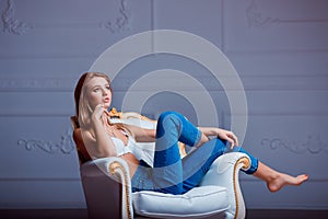 beautiful young woman posing on vintage chair. Girl in jeans and white bra.