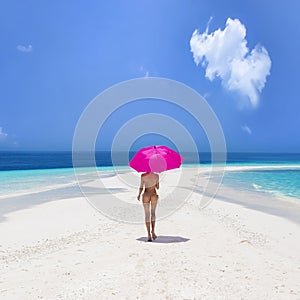 Sexy bikini body woman on paradise tropical beach having fun on Maldives. Beautiful female model is holding pink umbrella and is