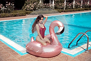 bikini girl model enjoying on inflatable giant pink flamingo pool float mattress in fashion swimwear. Attractive tanned woman