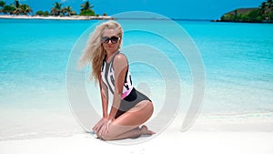 Sexy blond Woman in fashionable bikini suntanning on tropical beach. Pretty slim girl posing on exotic island by beautiful