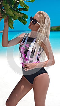 Sexy blond Woman in fashionable bikini suntanning on tropical beach. Pretty slim girl posing on exotic island by beautiful