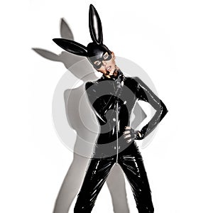 Sexy blonde beautiful woman posing in latex costume and black bunny mask on white background.