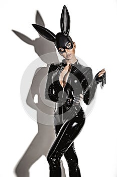 Sexy blonde beautiful woman posing in latex costume and black bunny mask on white background.