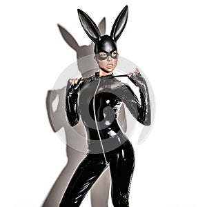 Sexy blonde beautiful woman posing in latex costume and black bunny mask on white background.