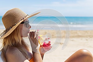 sexy blonde in a bright bikini is sunbathing on a sun lounger with a cocktail in her hand by the sea