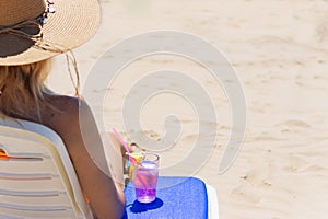 A sexy blonde in a bright bikini is sunbathing on a sun lounger with a cocktail in her hand by the sea. girl is enjoying
