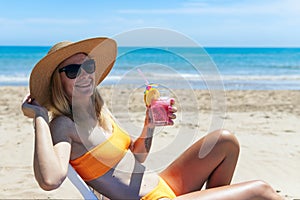 A sexy blonde in a bright bikini is sunbathing on a sun lounger with a cocktail in her hand by the sea. girl is enjoying
